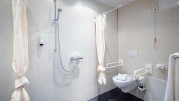 Un baño con ducha, inodoro y barras de apoyo.