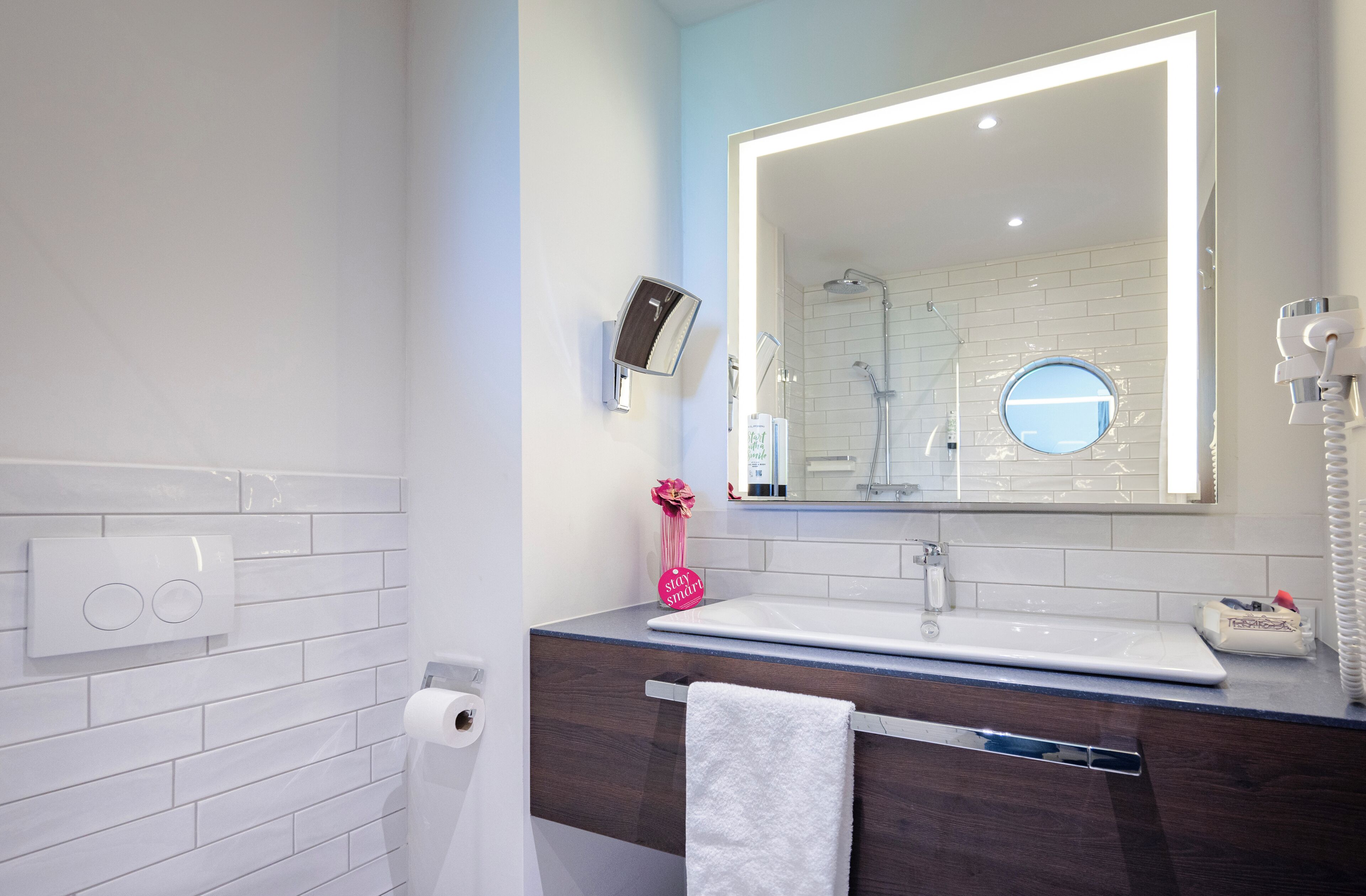 A bathroom with a white sink, a mirror, a towel rack, a toilet paper holder, and a shower area.