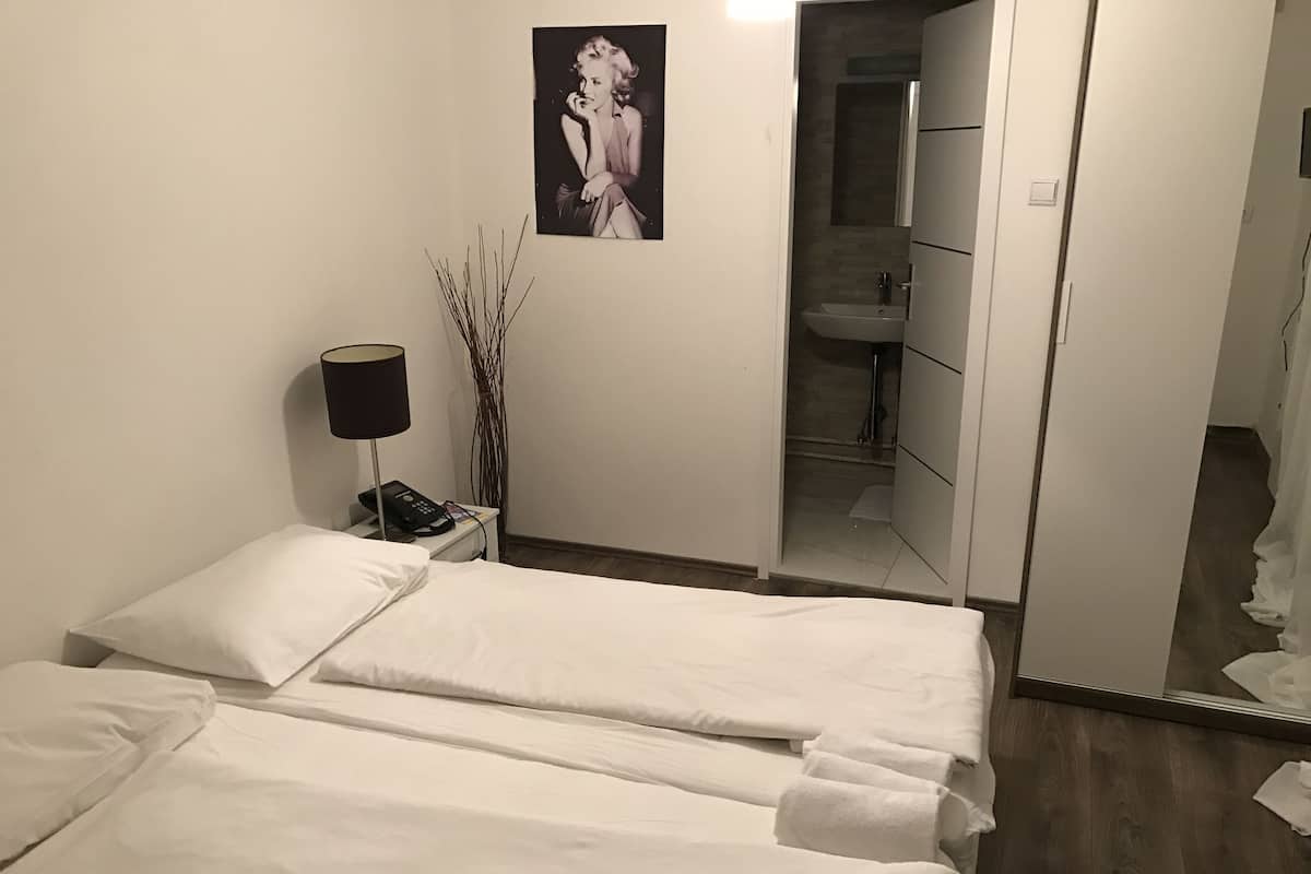 A hotel room with two beds, a bedside table with a lamp, a mirror, and a poster on the wall.