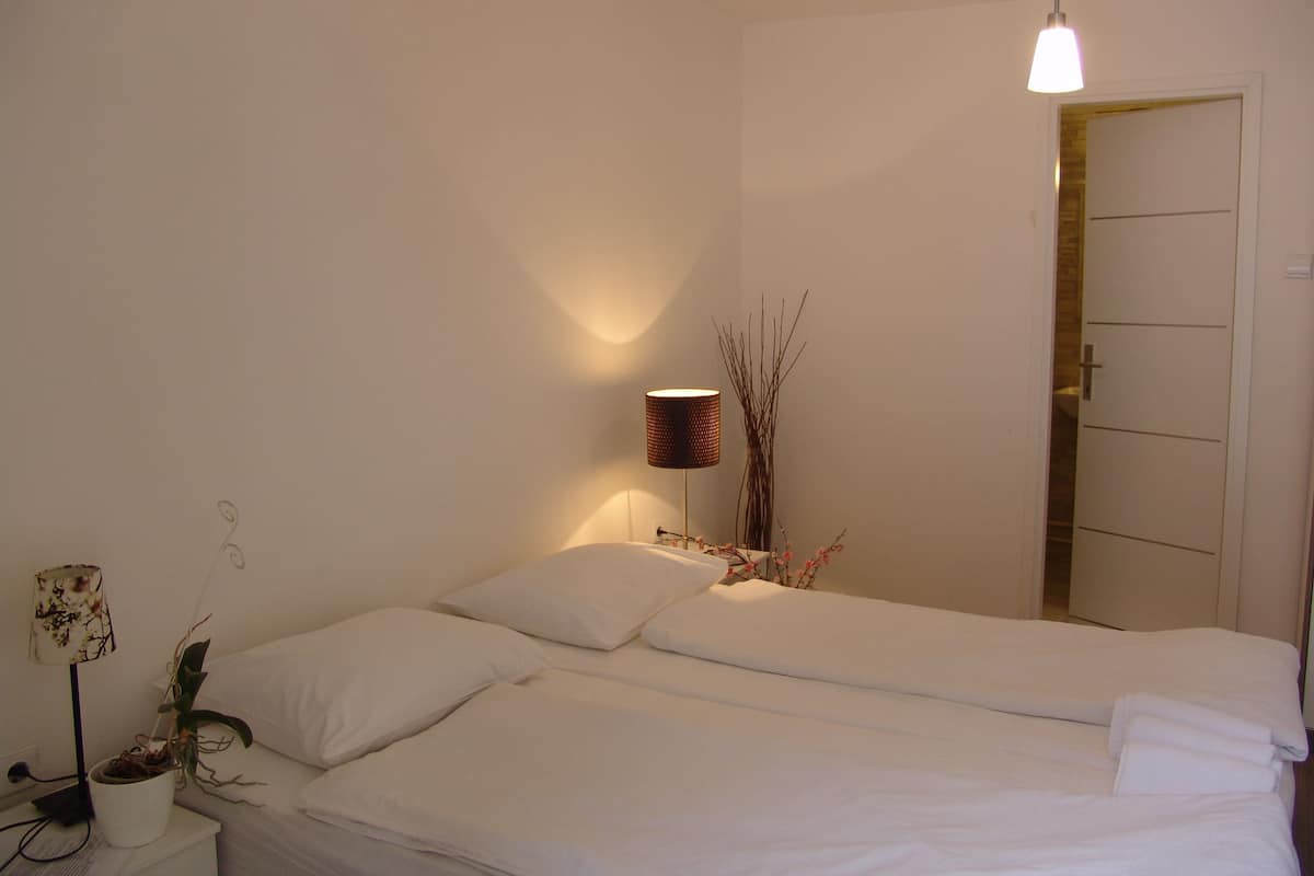 A neatly made bed with white linens, a bedside lamp, and a small potted plant.
