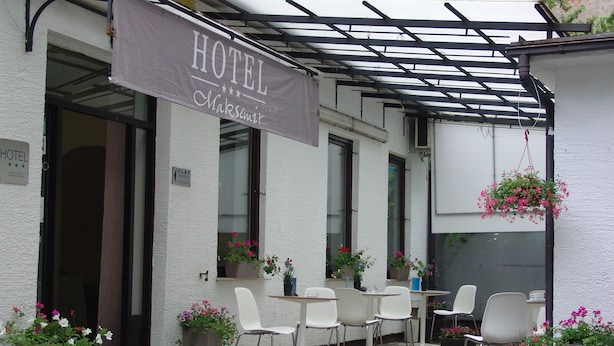 Ein Hotel mit einer überdachten Terrasse, Sitzgelegenheiten im Freien mit weißen Stühlen und hängenden Blumenkörben.