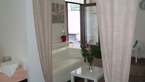 Ein Zimmer mit einem weißen Sofa, einem kleinen Tisch mit Blumenvase und einem Fenster mit Blick nach draußen.