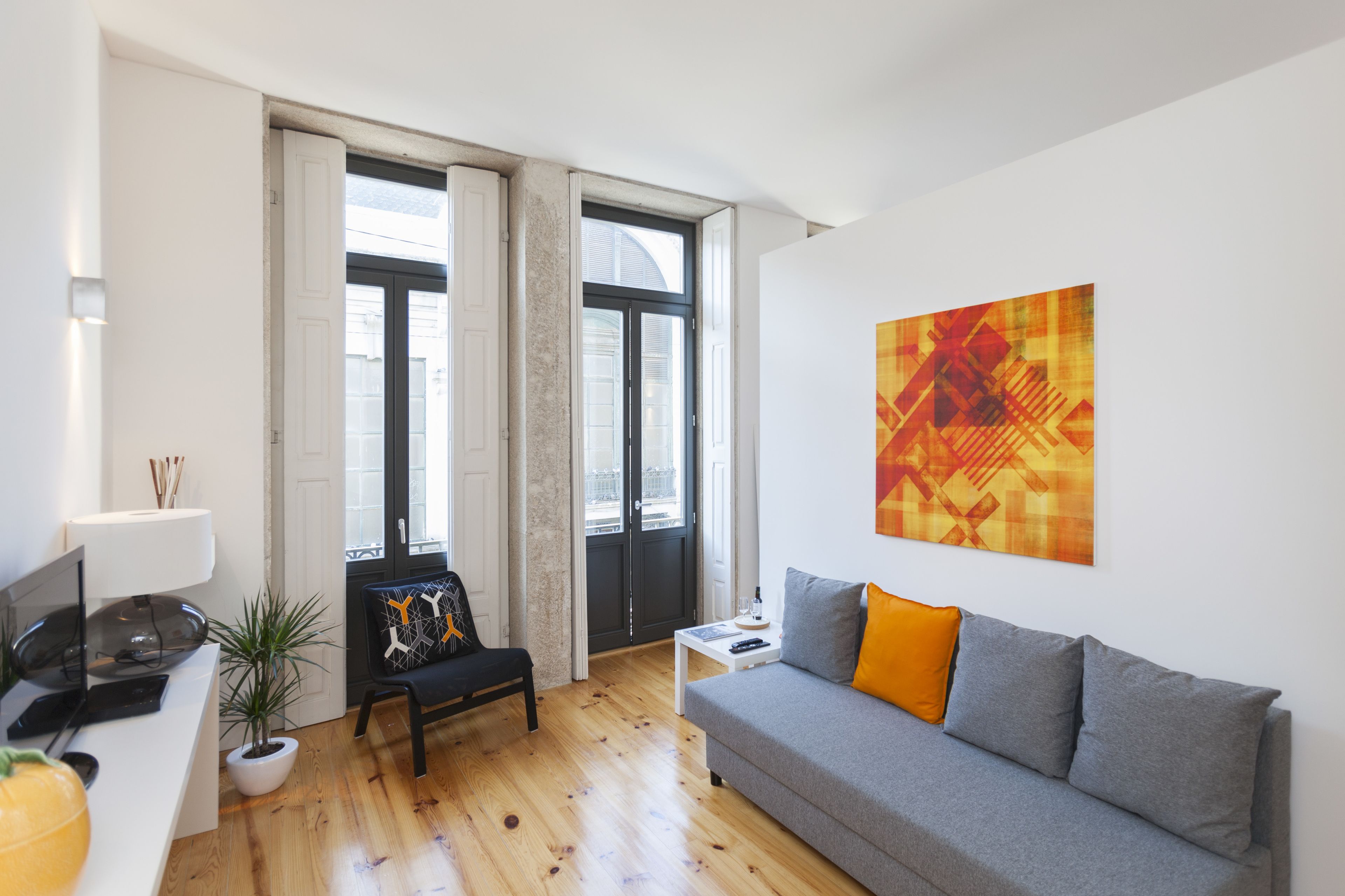 A modern living room with a grey sofa, a black chair, a white side table, and a potted plant.