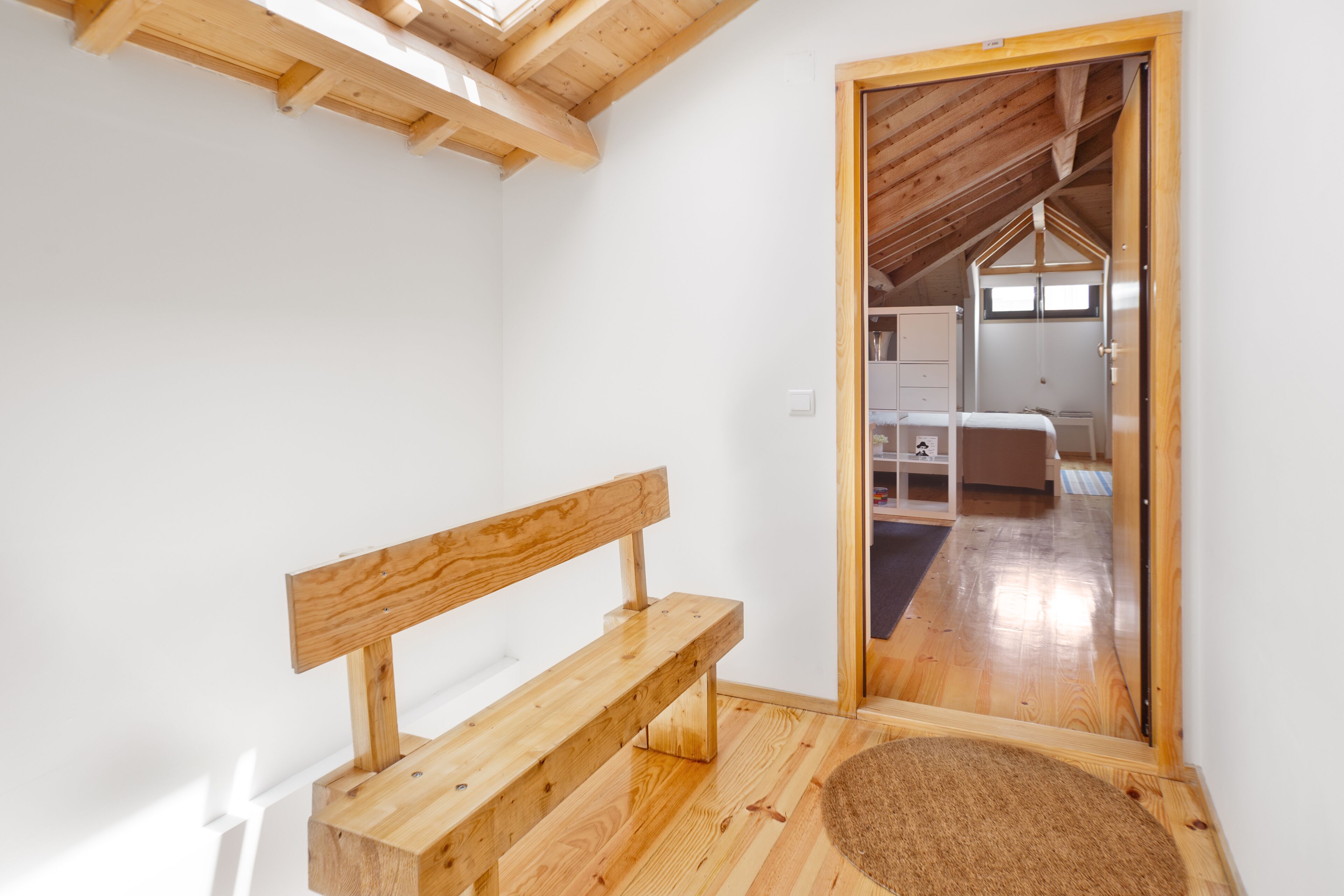 Un banco de madera en una habitación con techo inclinado y una puerta que da a otra estancia.
