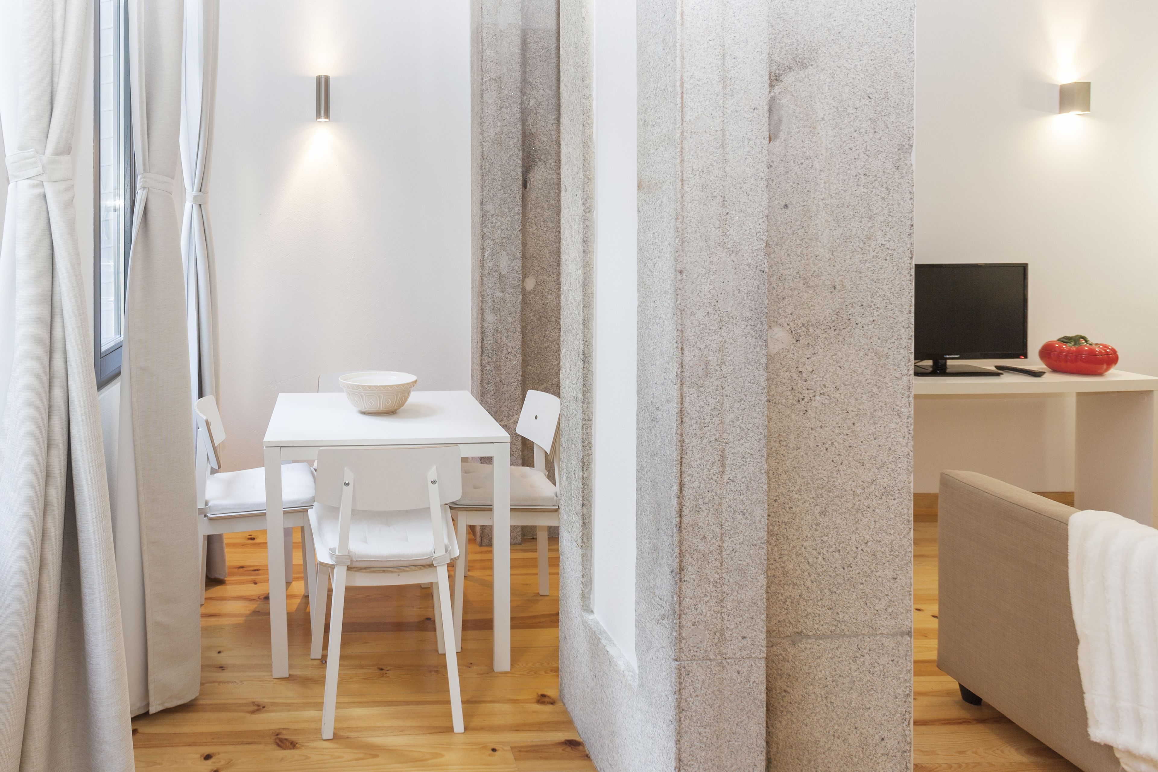 Une pièce moderne et minimaliste, avec une table et des chaises blanches, un téléviseur et un objet rouge posé sur une étagère.