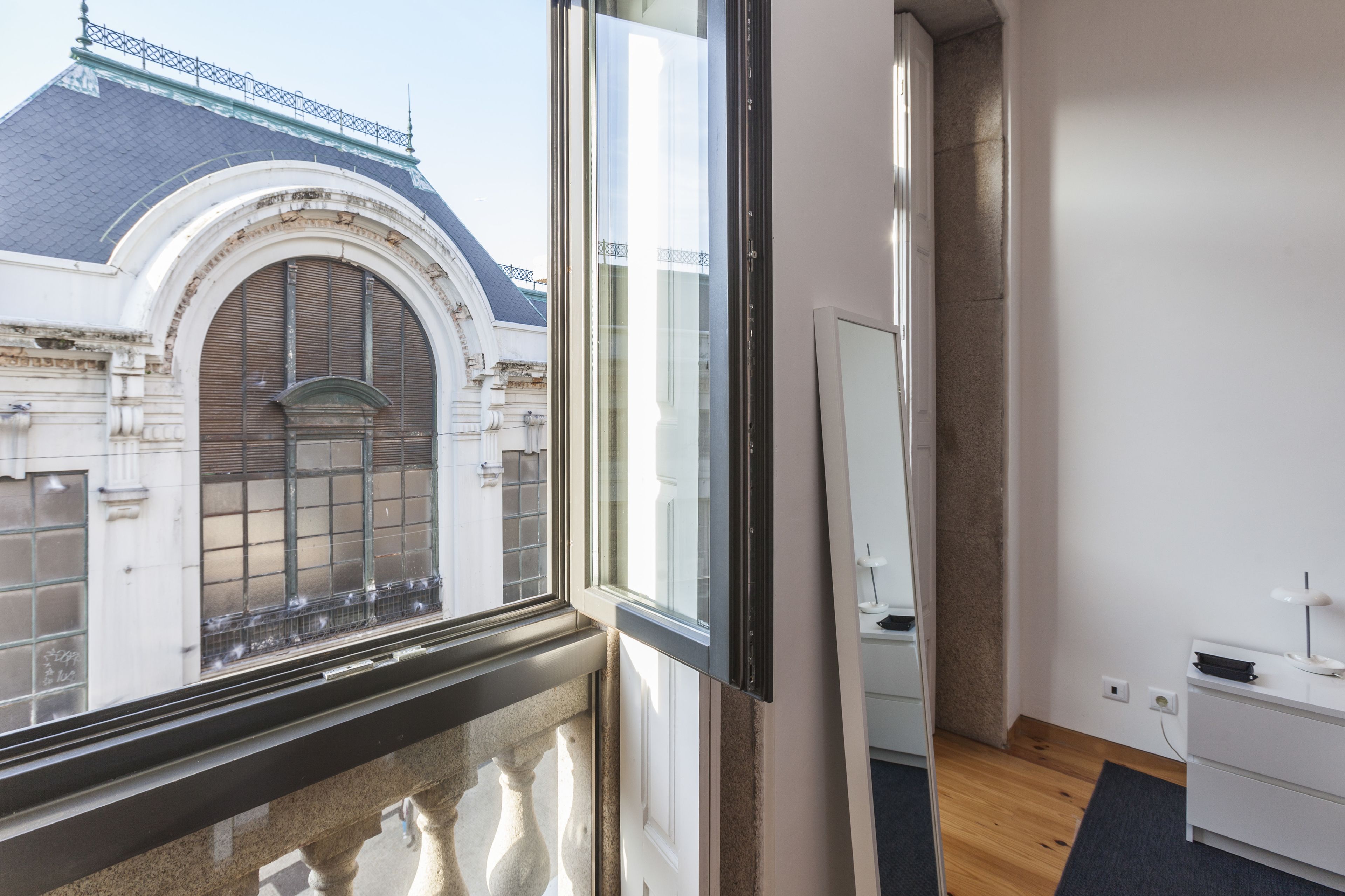 Ein Zimmer mit großem Fenster, das einen Blick auf ein historisches Gebäude mit Ziegeldach und Rundbogenfenstern freigibt.