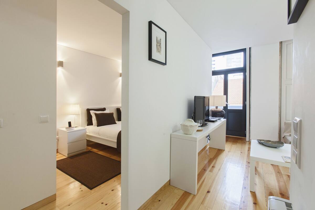 Une chambre moderne et bien éclairée, équipée d’un lit, d’une table de chevet et d’un petit bureau avec une télévision.