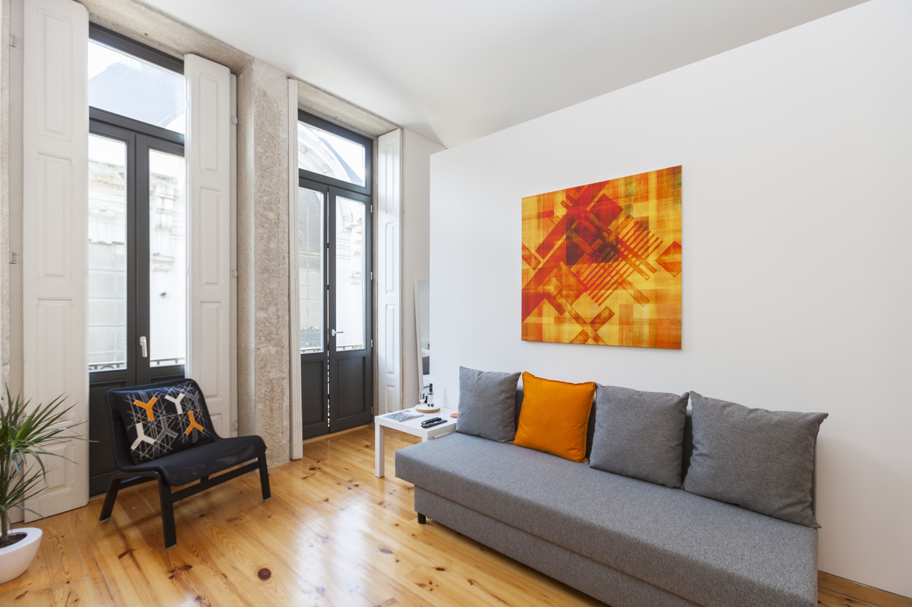 A modern living room with a grey sofa, a black chair with a geometric cushion, a small white table, and a large abstract painting on the wall.
