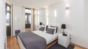A modern bedroom with a large bed, bedside tables, and a view of the outdoors. - BO - Bolhão Apartments (Porto)