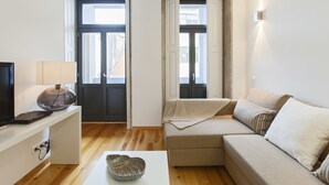 A modern living room with a sofa, a coffee table, and a television on a stand. - BO - Bolhão Apartments (Porto)