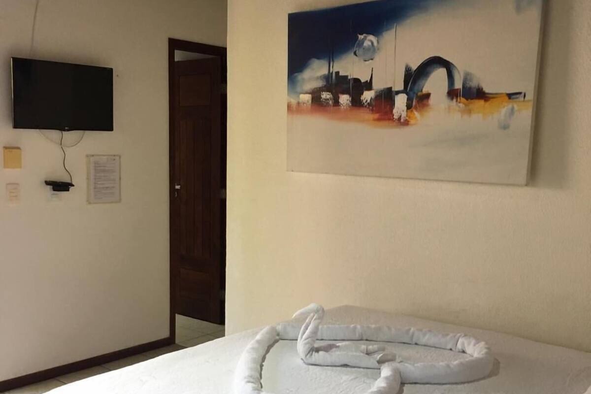 A hotel room with a bed, a painting on the wall, a television, and a door.