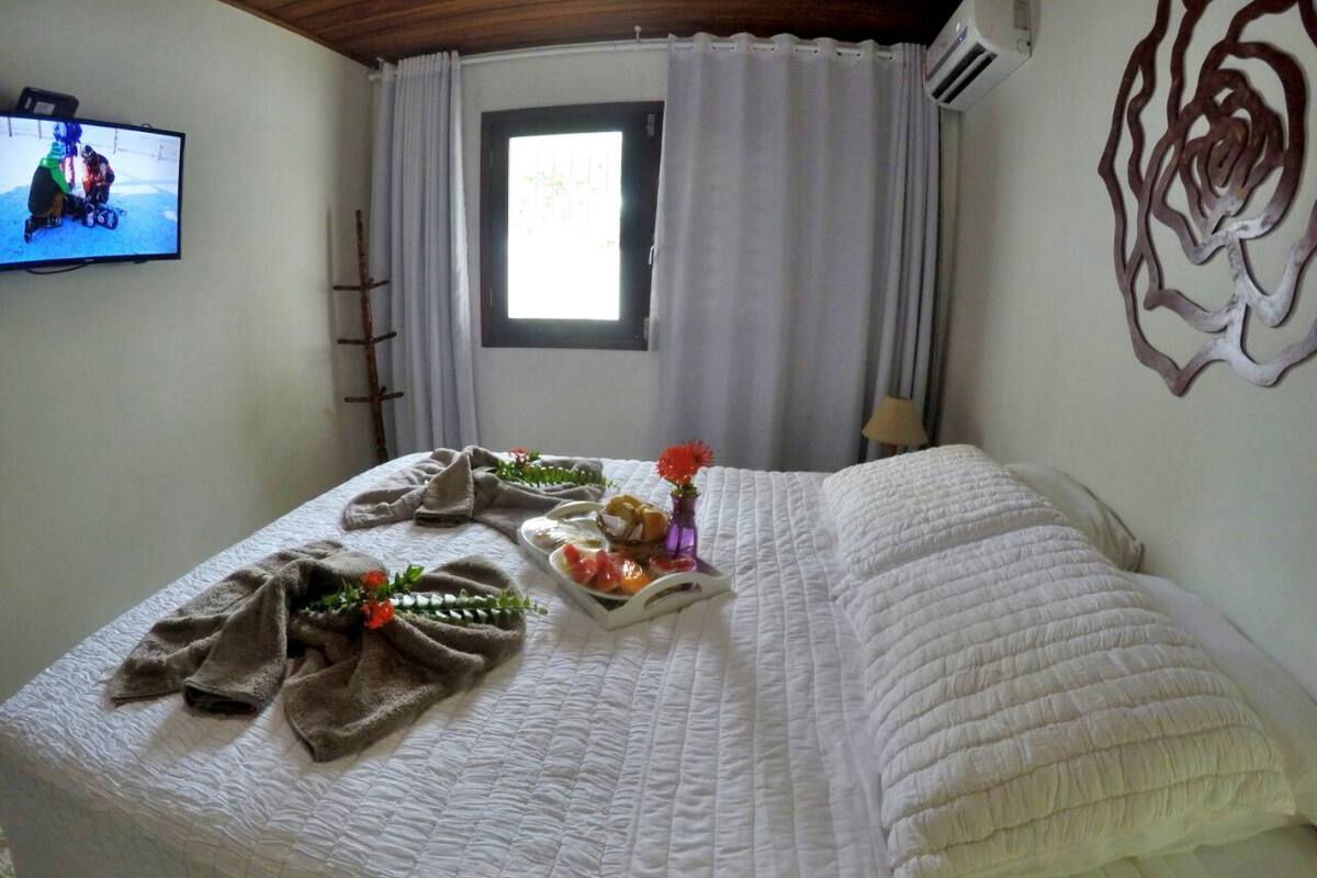 A neatly made bed with a white quilt, a tray of breakfast items, and a vase of flowers.