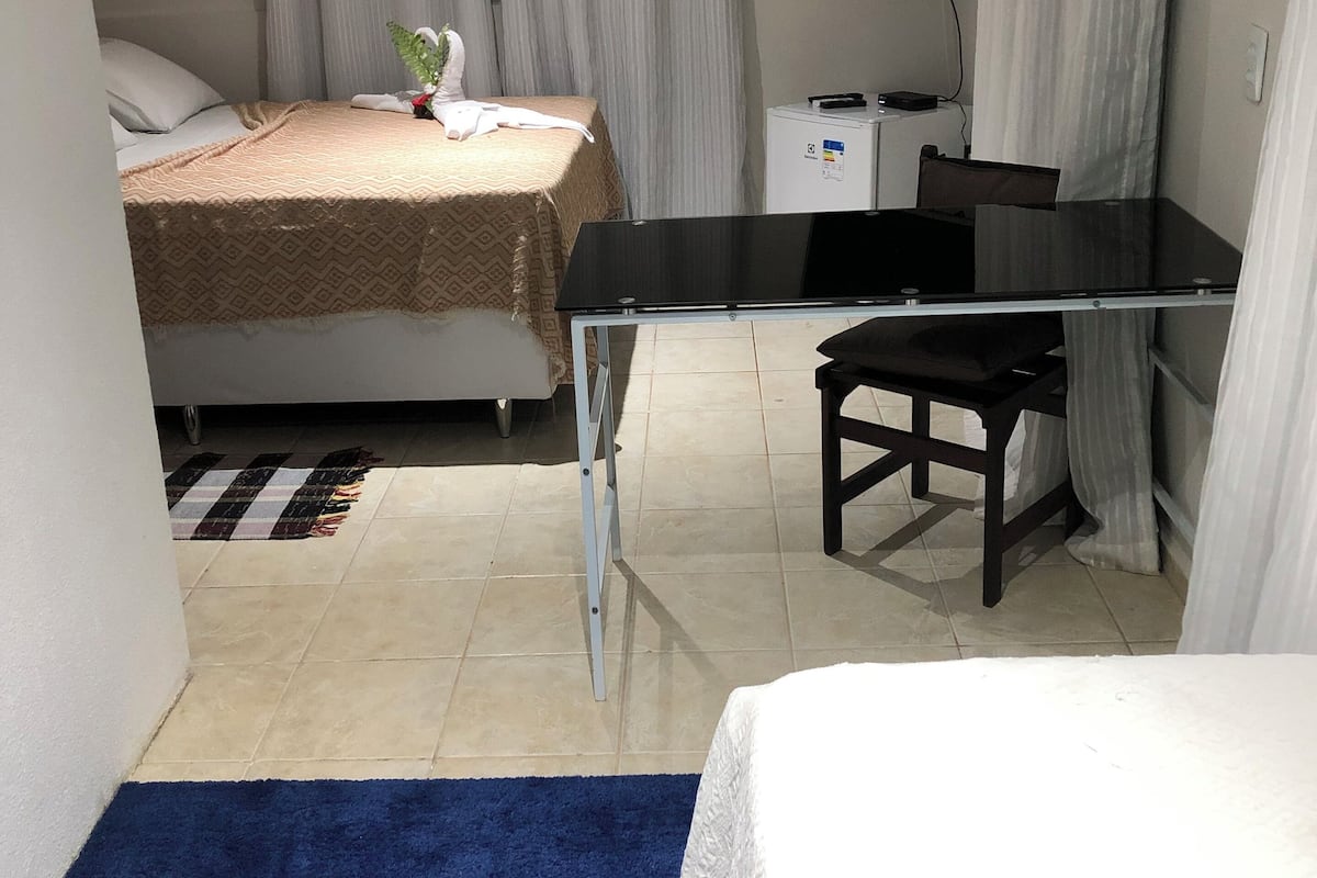 A hotel room with a bed, a desk, a chair, a TV, and a small refrigerator.