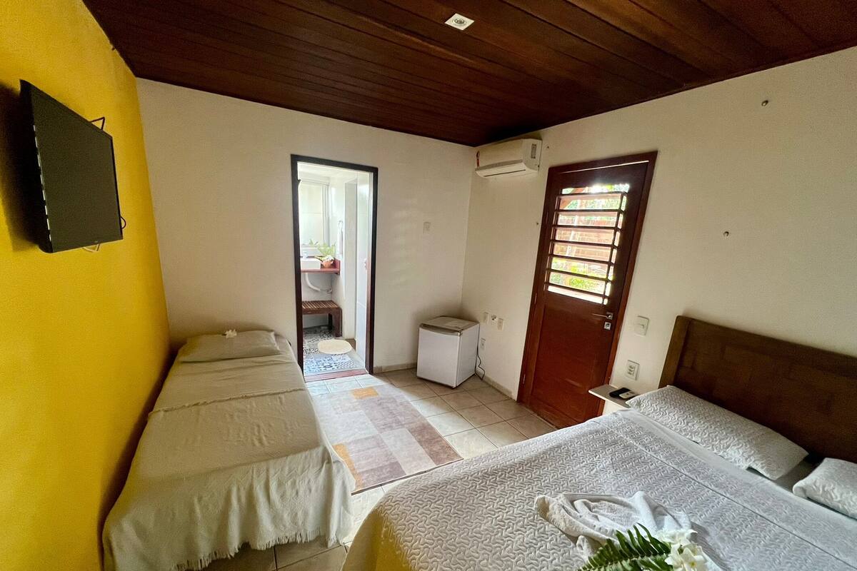 A room with two beds, a small table, a chair, a door, and an air conditioning unit.