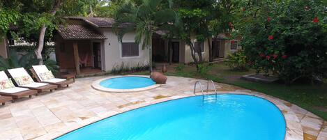 A swimming pool with lounge chairs and a small house in the background.