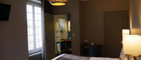 Un dormitorio con cama, lámpara de noche, ventana y puerta.