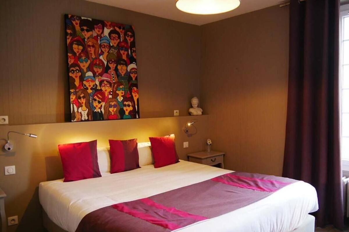 Een hotelkamer met een groot bed, een hoofdbord met verlichting, een aan de muur hangend schilderij, een nachtkastje en een raam met gordijnen.