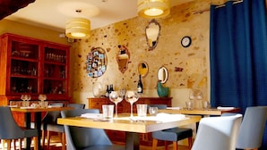 A dining area with wooden tables and blue chairs, a wooden cabinet with glassware, and a wall with decorative mirrors and a clock. - Auberge de l'Abbaye (Thiron-Gardais)