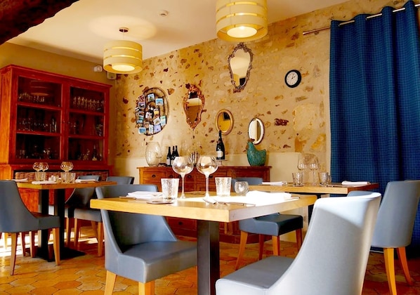 A dining area with wooden tables and blue chairs, a wooden cabinet with glassware, and a wall with decorative mirrors and a clock.