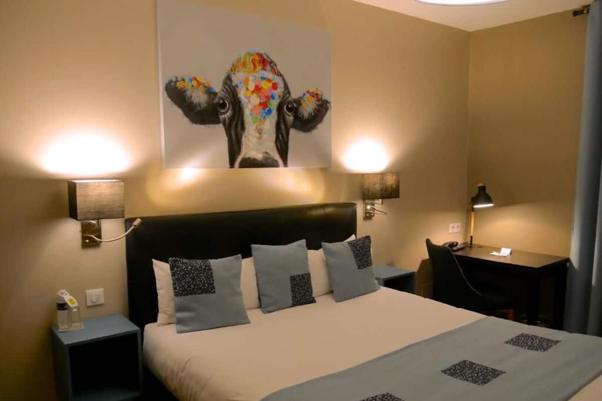 Een hotelkamer met een bed, twee nachtkastjes, een bureau en een schilderij dat aan de muur hangt.