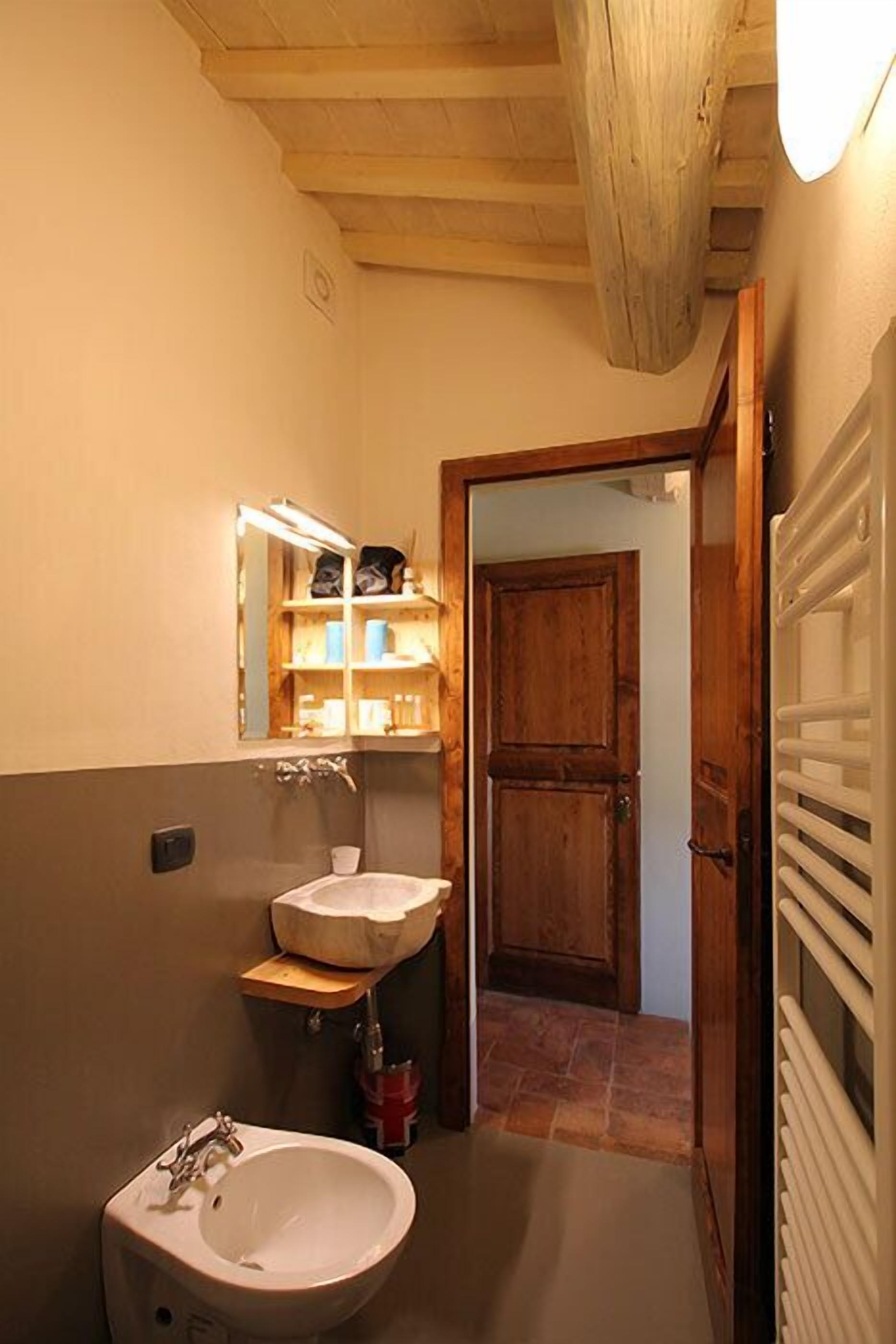 Une salle de bain avec un meuble-lavabo en bois, un lavabo blanc et un miroir doté d’étagères.