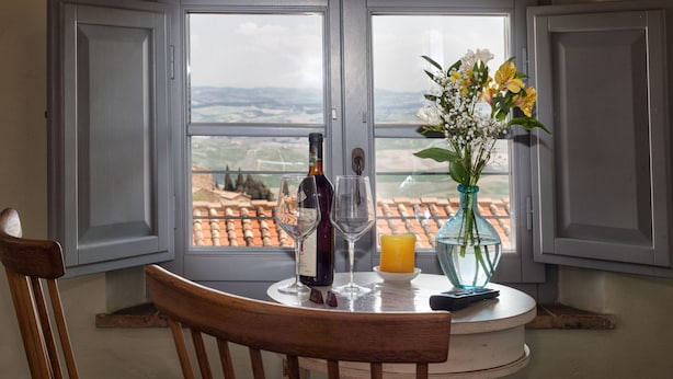 Une table à manger avec une bouteille de vin, deux verres à vin, une bougie et un vase rempli de fleurs.