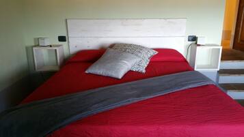 A bed with a red bedspread, a grey blanket, and patterned pillows. There are two bedside tables with lamps.