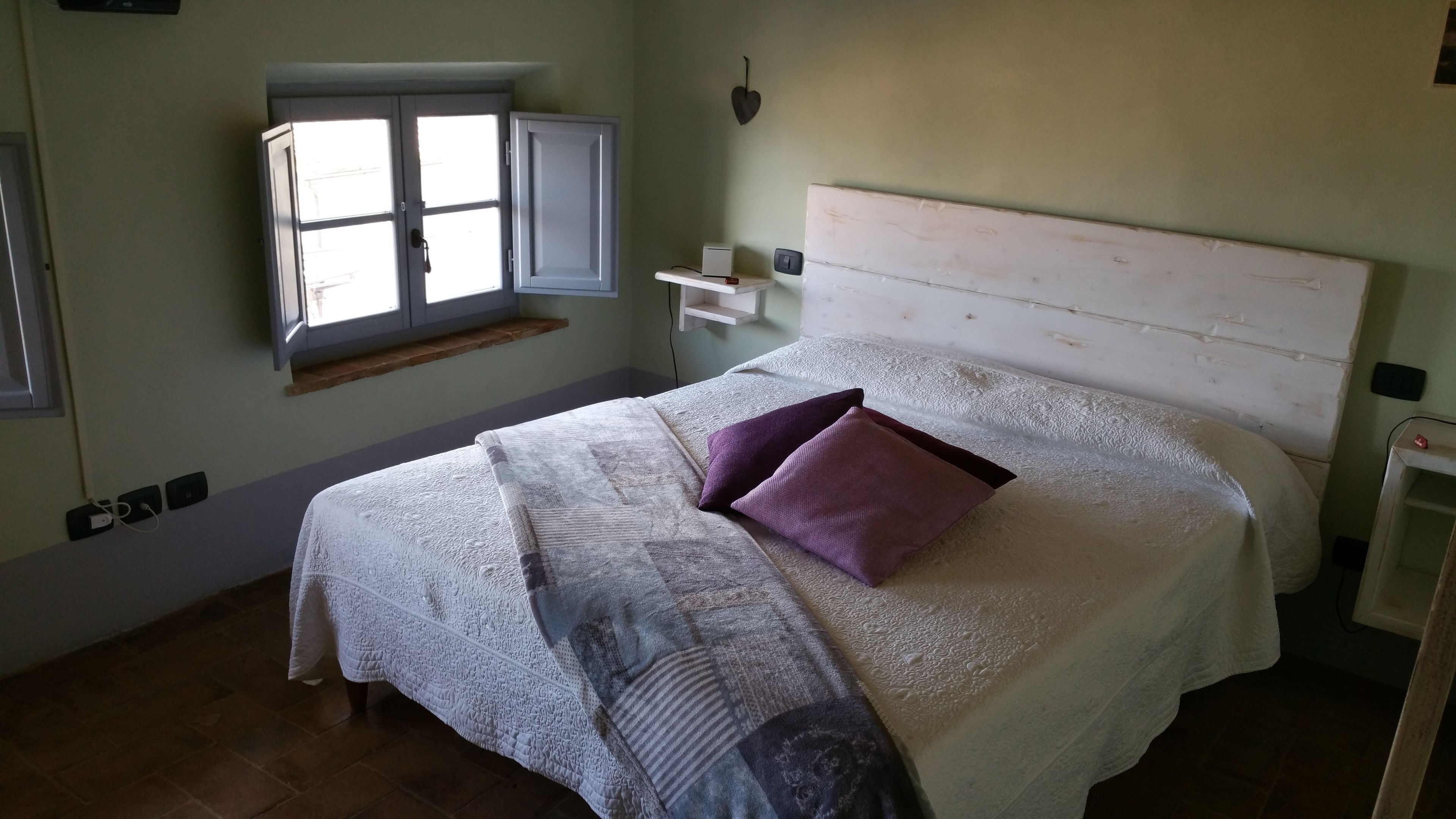 Une chambre à coucher avec un lit, une fenêtre, une étagère et un luminaire fixé au mur.