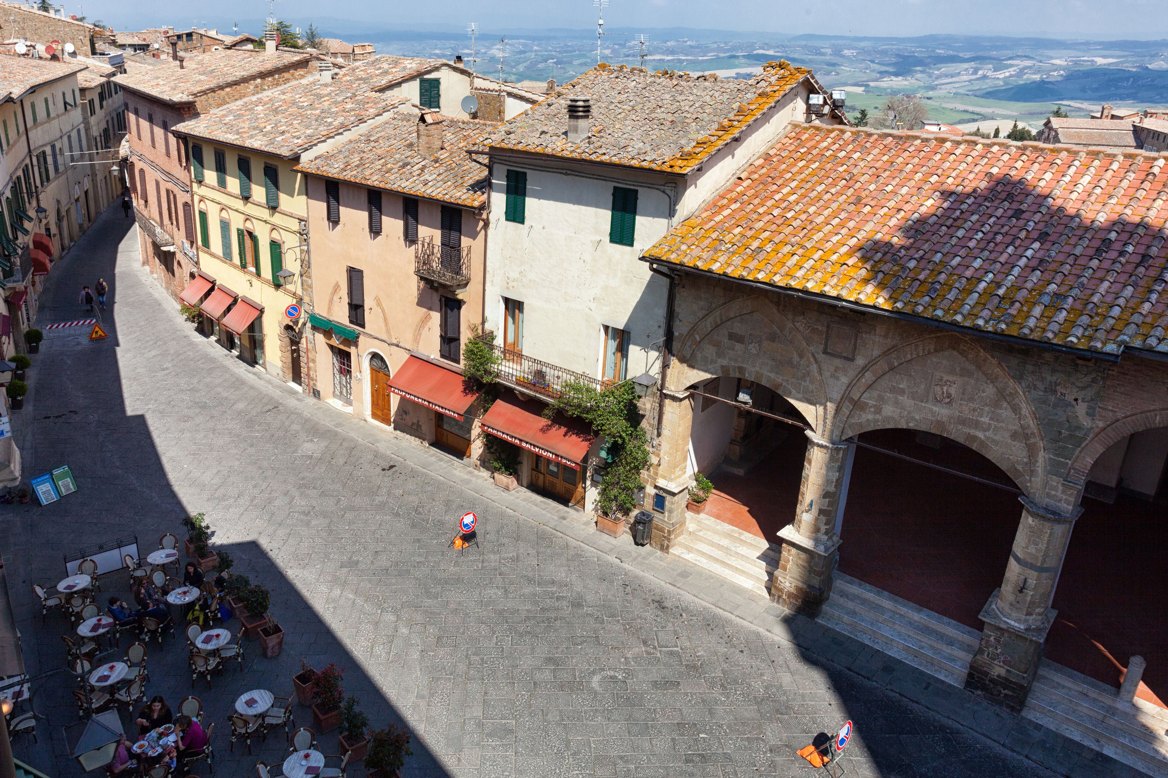 Une rue pavée bordée de bâtiments historiques, avec des terrasses et un arc en pierre.