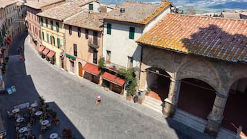 Une rue pavée bordée de bâtiments historiques, avec des terrasses et un arc en pierre.