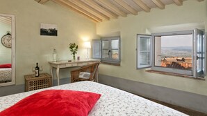Une chambre à coucher comprenant un lit, un bureau, une chaise, une fenêtre donnant sur un paysage agréable et une horloge murale.