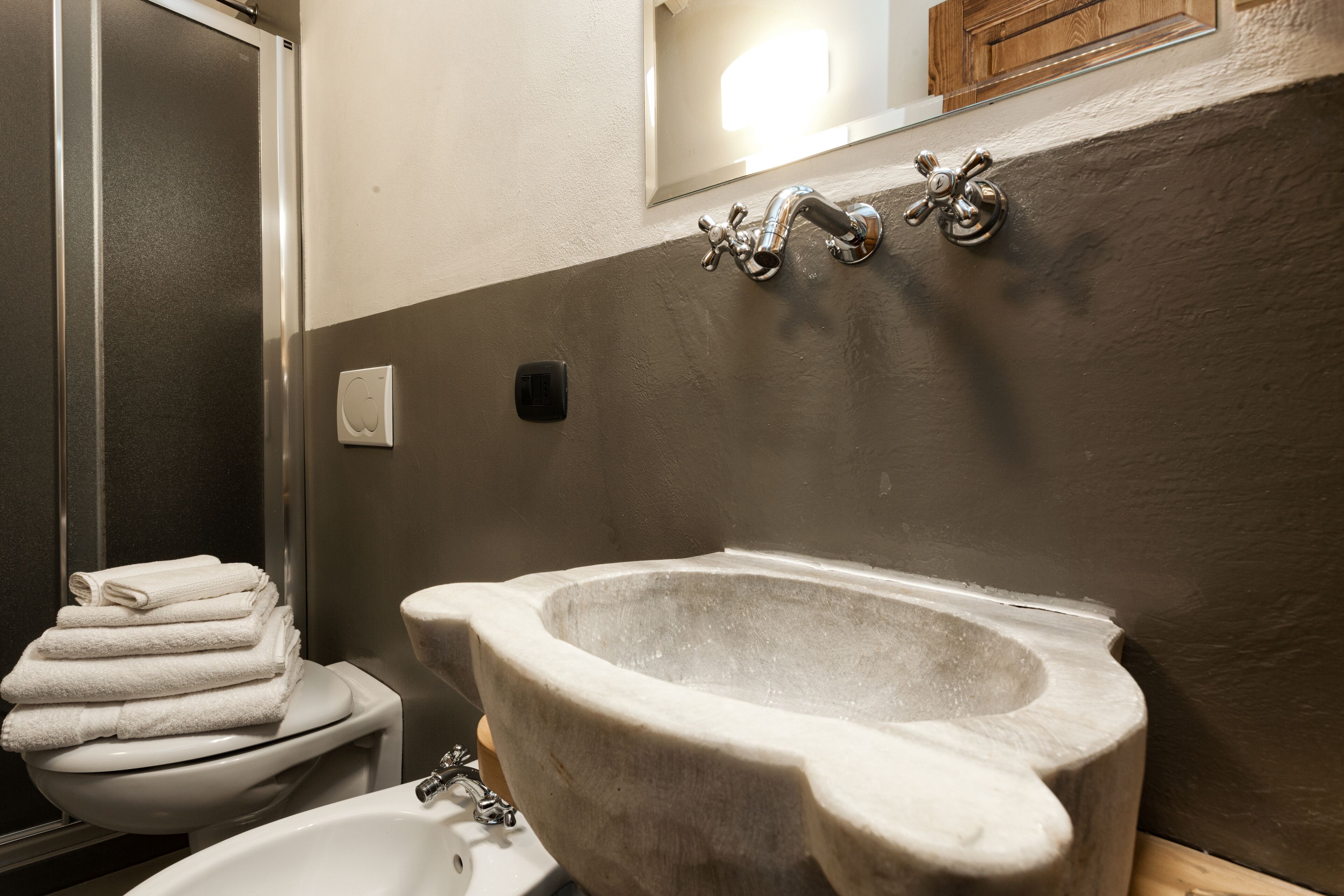 Une salle de bain avec un lavabo en marbre, des toilettes avec une pile de serviettes et un espace douche.