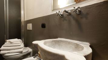 Une salle de bain avec un lavabo en marbre, des toilettes avec une pile de serviettes et un espace douche.