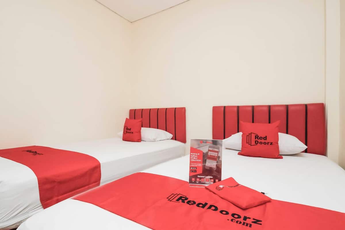 Habitación de hotel con dos camas, cada una con cabecero rojo y almohadas a juego. Un folleto está sobre la cama.