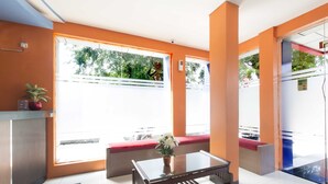 Un espace d’accueil comprenant une table en verre, un banc avec un coussin rouge et une plante en pot.