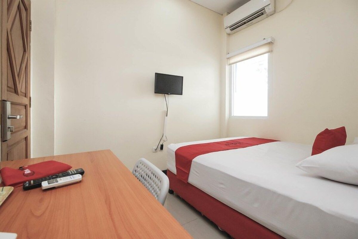 Een hotelkamer met een bed, bureau, stoel, televisie aan de muur en een raam.