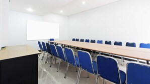 Une salle de conférence avec une longue table, des chaises bleues, un écran de projection et un tableau blanc.