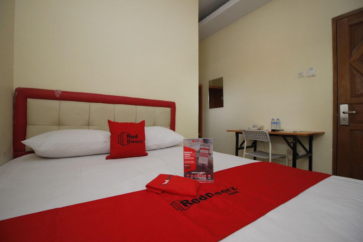 Een hotelkamer met een bed, een bureau en een stoel. Er ligt een kussen met het logo van het hotel en een brochure op het bed.