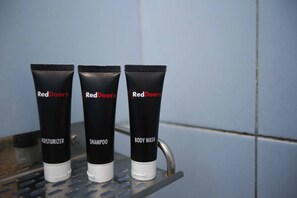 Three RedDoorz products: a moisturizer, shampoo, and body wash, on a metal shelf against a tiled wall.