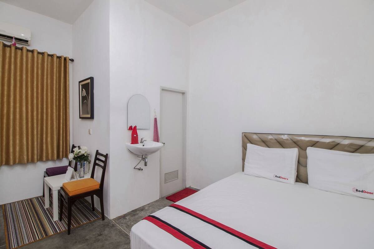 A hotel room with a bed, a chair, a small table, a sink, and a window with curtains.