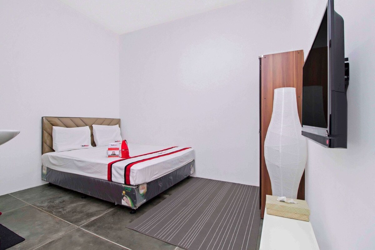 A hotel room with a bed, a TV mounted on the wall, and a large vase on a table.