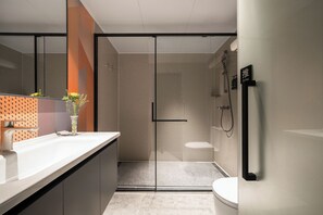 Ein modernes Badezimmer mit einer gläsernen Duschkabine, Toilette und Waschbecken mit Blumen in einer Vase.