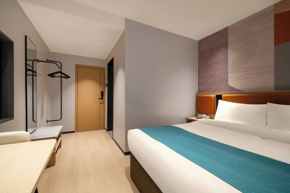 Habitación de hotel con cama, escritorio, espejo, armario y televisor montado en la pared.