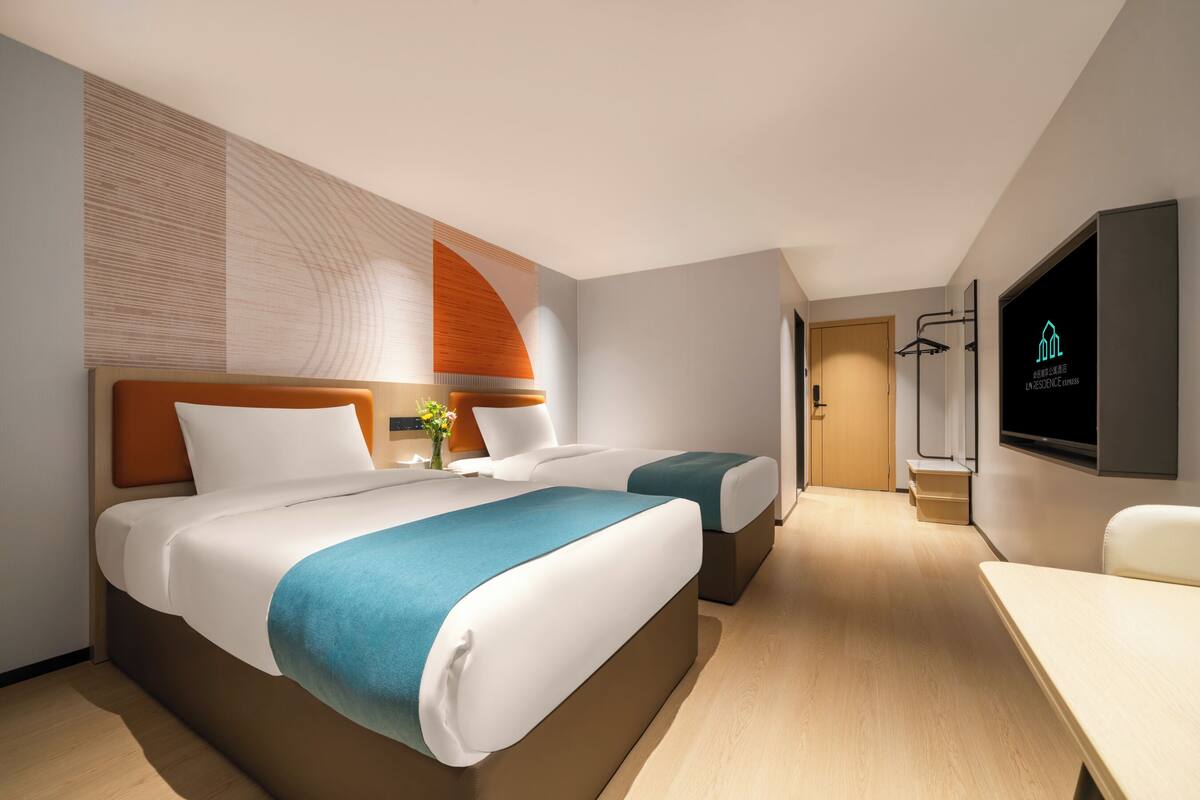 Una habitación de hotel moderna con dos camas, un televisor de pantalla plana, piso de madera y diseño minimalista.