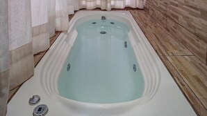A spa room with a large bathtub, a wooden ceiling, and a tiled wall. - Fazenda Pousada das Palmeiras (Brotas)