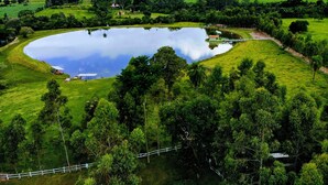 A large, circular pond surrounded by lush green fields and trees. - Fazenda Pousada das Palmeiras (Brotas)