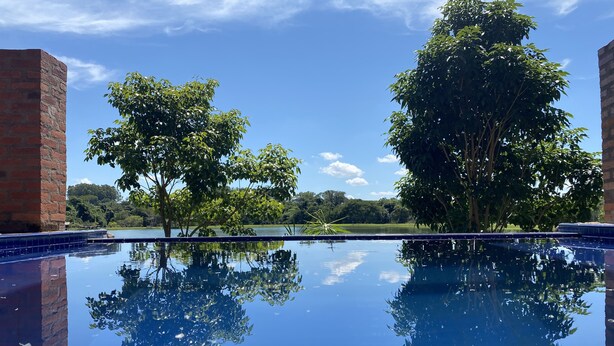 A clear view of a swimming pool with a reflection of trees and a distant landscape. - Fazenda Pousada das Palmeiras (Brotas)