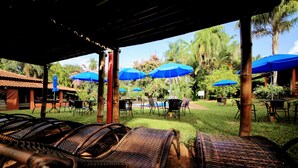 An outdoor seating area with wicker chairs and blue umbrellas, surrounded by greenery and palm trees. - Fazenda Pousada das Palmeiras (Brotas)