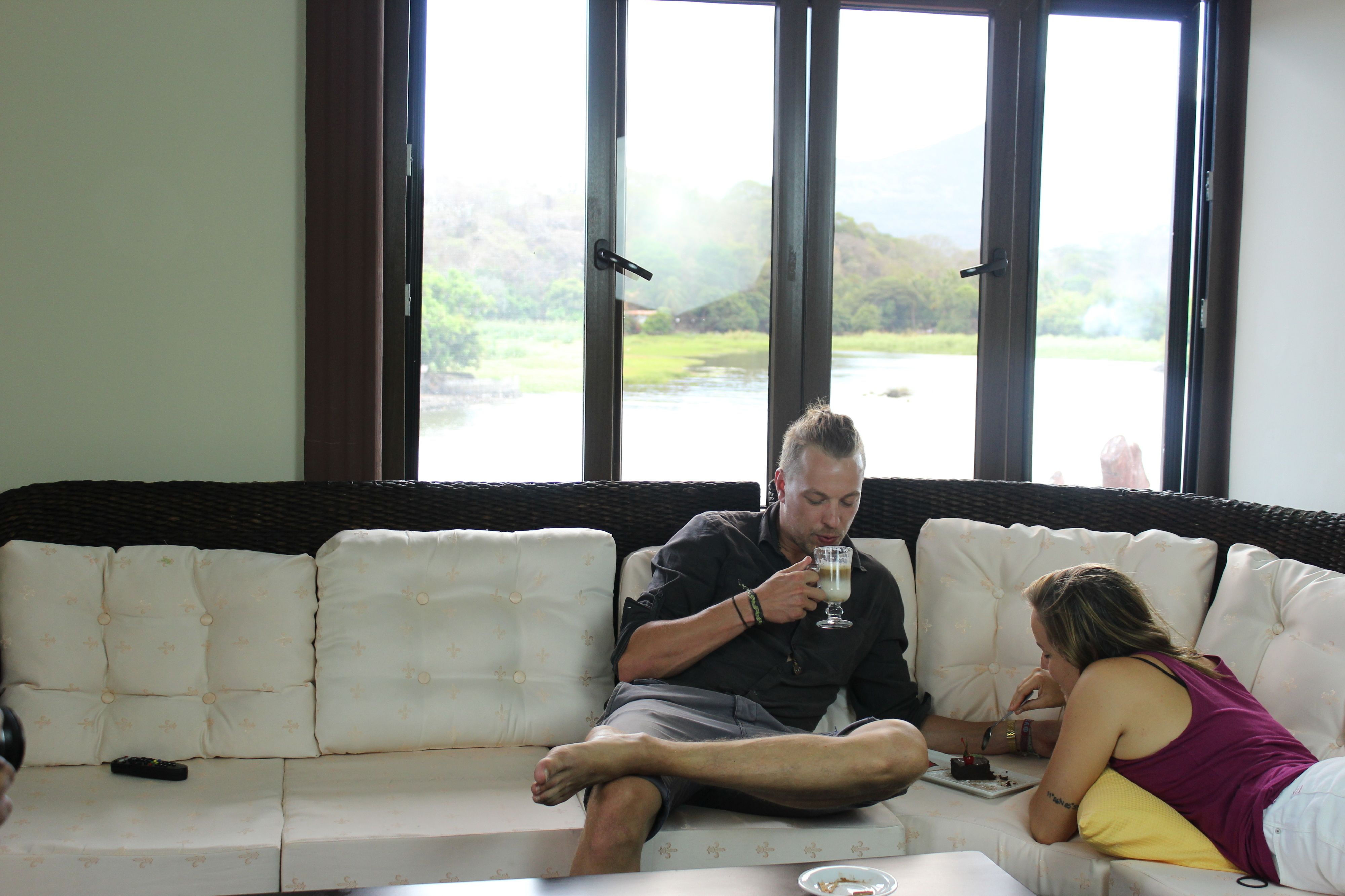 A man and a woman sitting on a white sofa with a remote control on it.
