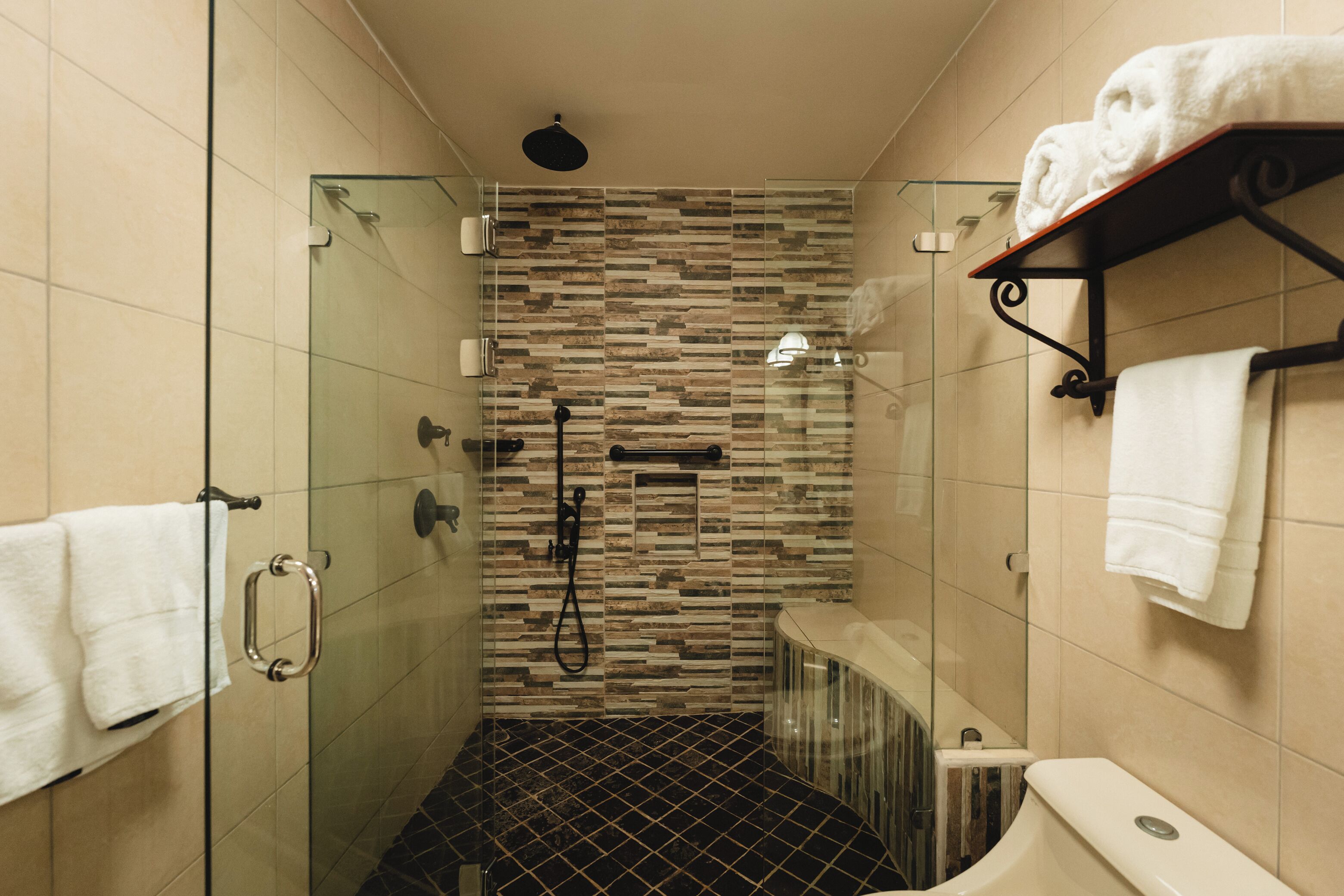 Um banheiro moderno com chuveiro em cabine de vidro, piso com padrão preto e branco e parede revestida com azulejos bege.